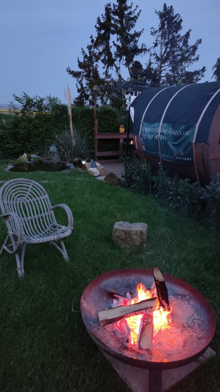 Mobile Sauna im Garten in der Dämmerung, davor ein Lagerfeuer