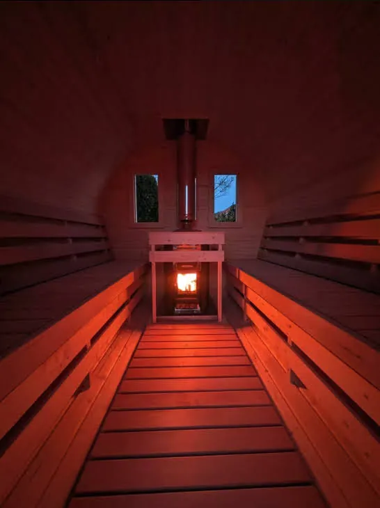 Innenraum der Fasssauna mit warmer Ambientebeleuchtung und Ofenfeuer