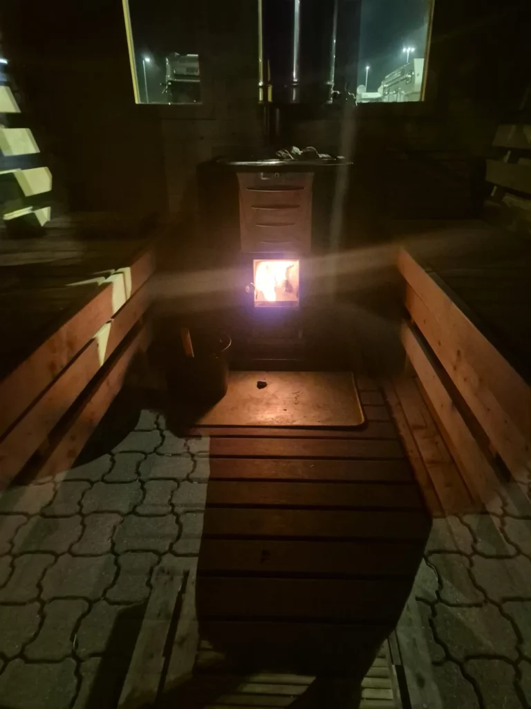 Fasssauna am Abend: Blick durch die offene Tür auf das Ofenfeuer