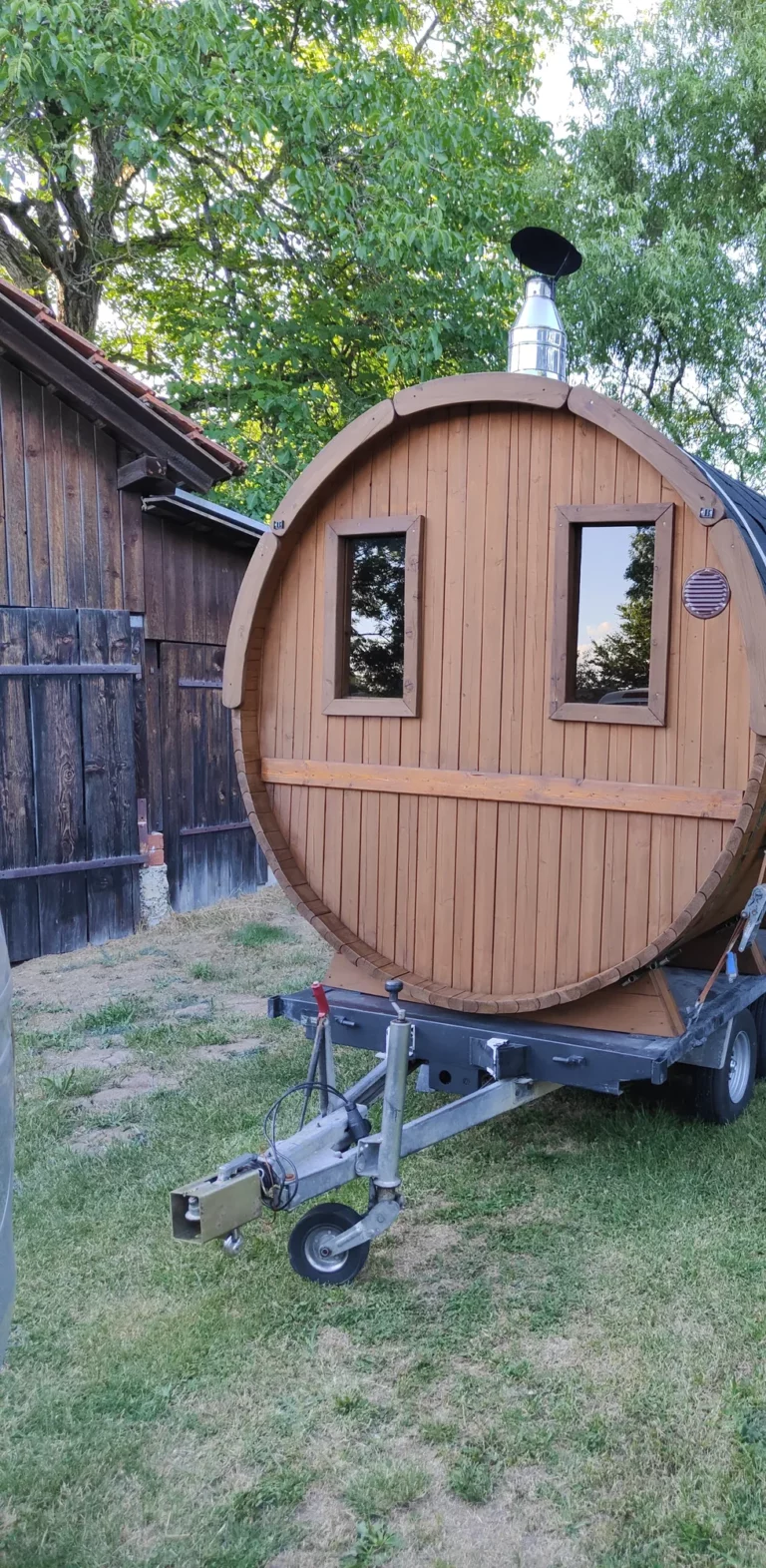 Mobile Fasssauna auf dem Anhänger im Garten neben einer Scheune