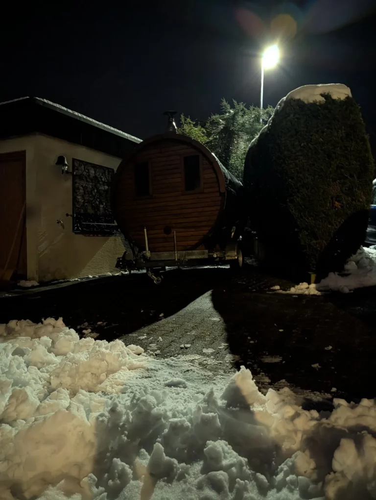 Mobile Fasssauna in einer verschneiten Einfahrt bei Nacht
