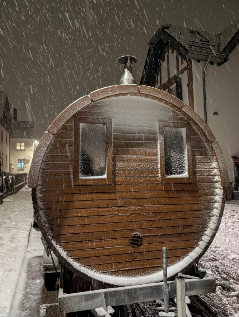 Fasssauna im Schneefall bei Nacht
