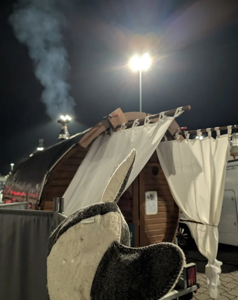 Saunahut vor der beleuchteten Fasssauna bei Nacht